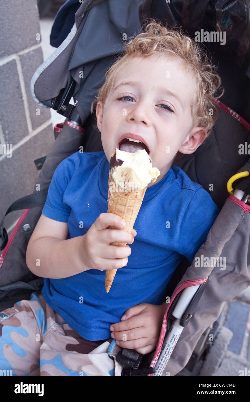 Three year old boy in a pushchair eating a large ice cream Stock Photo Alamy