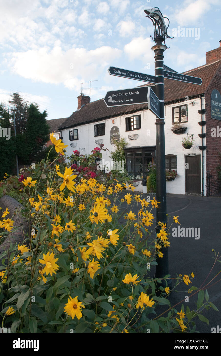 Bright yellow daises and a fingerpost infront of an old cottage and