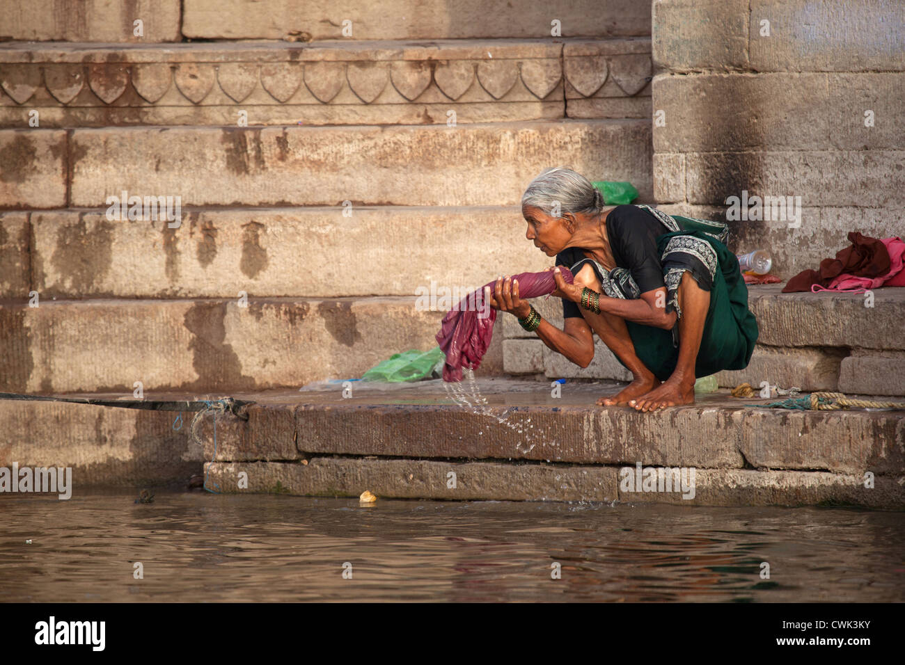 Old washerwoman washing linen in polluted water of the Ganges river at Varanasi, Uttar Pradesh, India Stock Photo