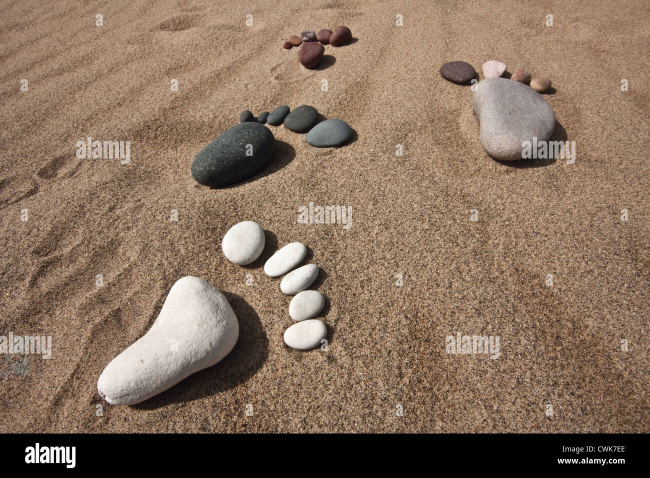 different coloured footsteps made from pebbles take a united walk across a sandy beach Stock Photo