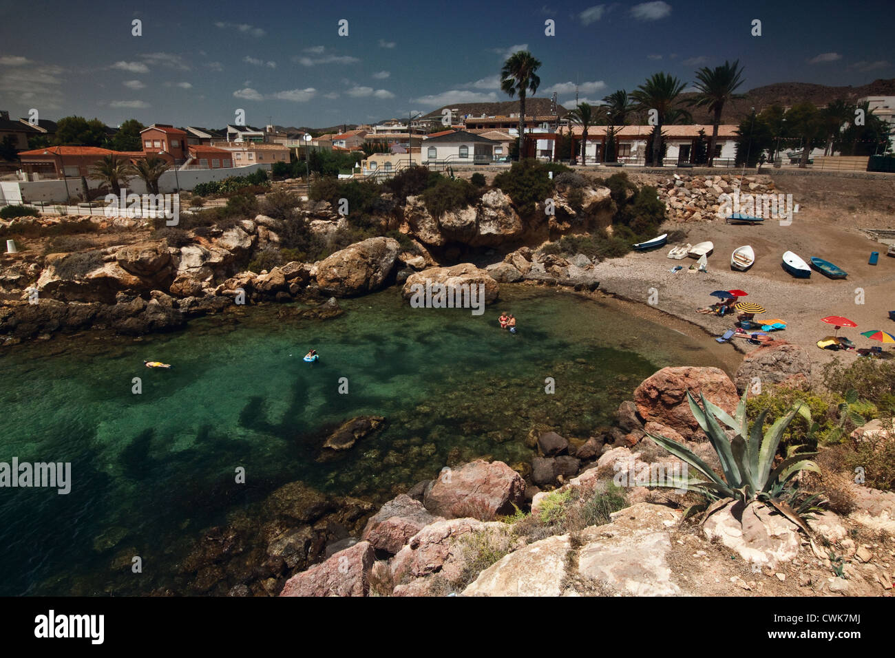 bathers and sun worshipers enjoying the Mediterranean sun in a small cove at Isla Plana with distant palm trees. Near Mazarron Stock Photo