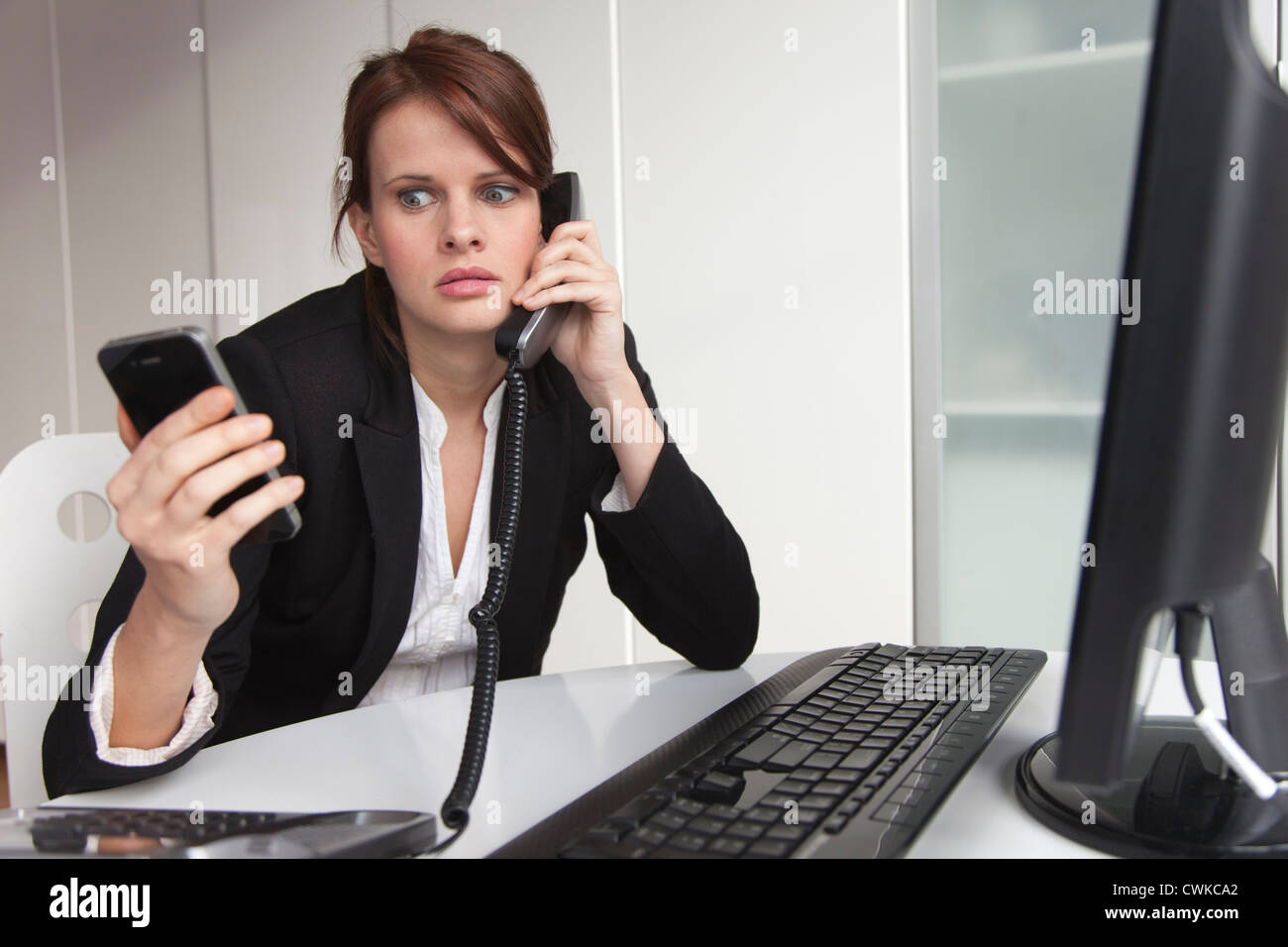 Businesswoman holding cell phone and talking on landline phone Stock Photo