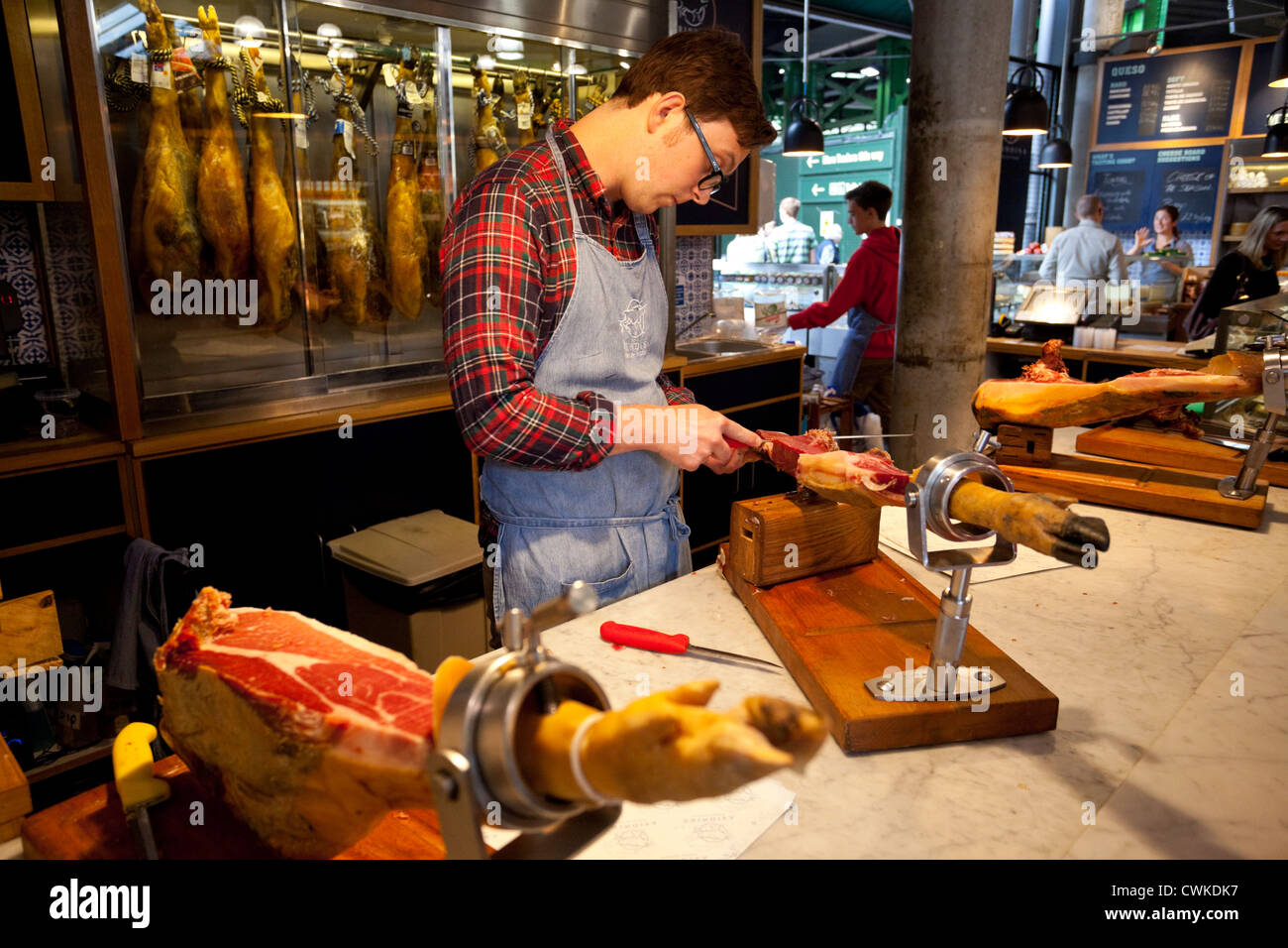 A man carves an Iberian ham (jamón) leg into slices, Borough Market, London, England, UK Stock Photo