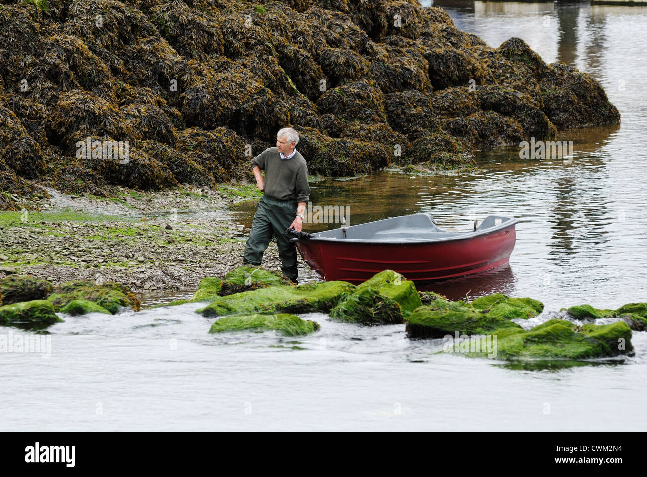 Man wearing waterproof trousers, holding a small boat at the waters edge, Aberystwyth, Wales. Stock Photo