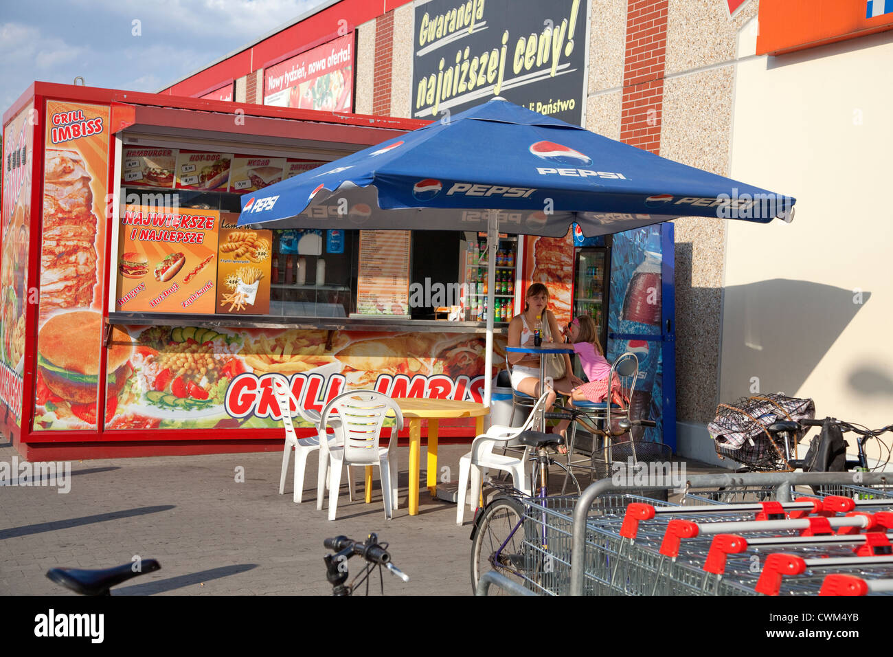 Mom and daughter enjoying a snack in a sidewalk cafe under an umbrella by  large supermarket. Tomaszow Mazowiecki Central Poland Stock Photo - Alamy