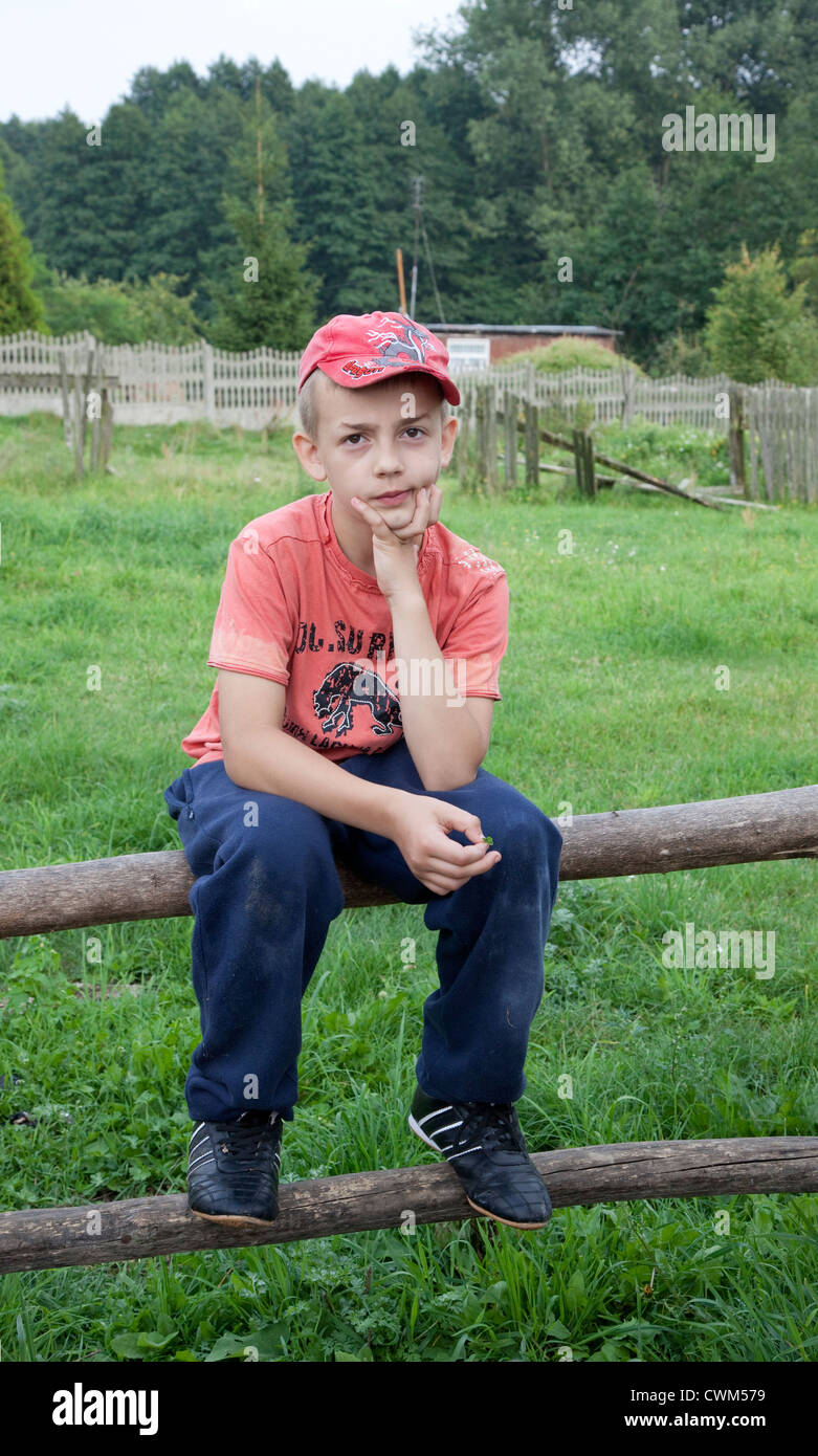 Polish boy age 10 from the village sitting on log fence surrounding a small field. Mala Wola Central Poland Stock Photo
