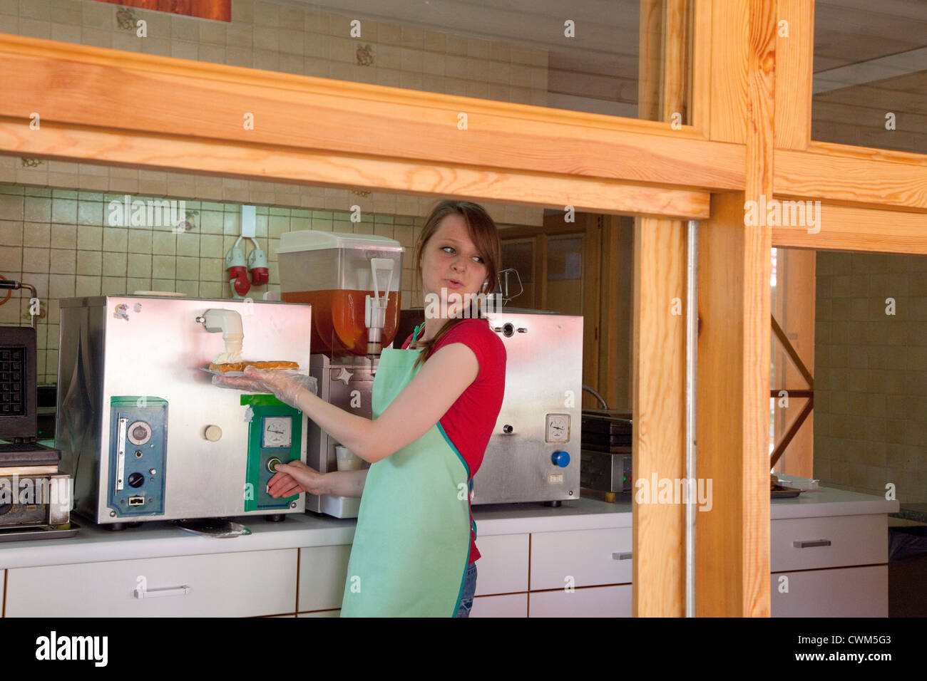 Shop attendant adding whipped cream to a waffle in a sidewalk kiosk. Spala Central Poland Stock Photo