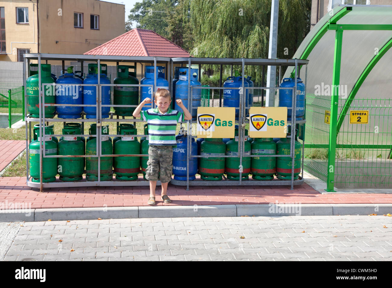 Macho young Polish lad age 6 showing his biceps muscles in front of gas tanks at petrol station. Rzeczyca Central Poland Stock Photo