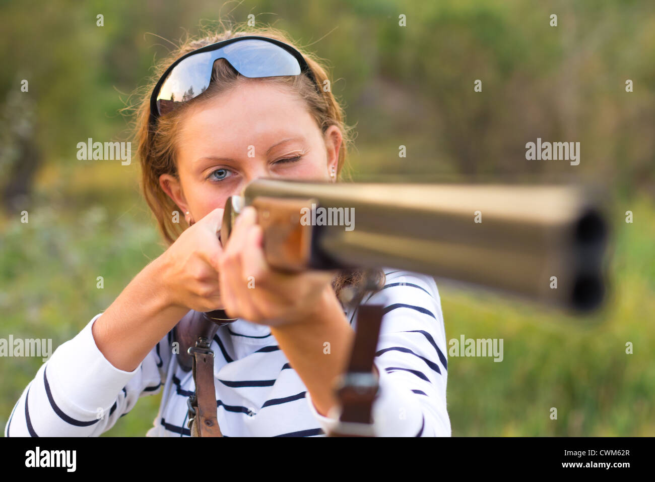 A young girl with a gun for trap shooting and shooting glasses aiming