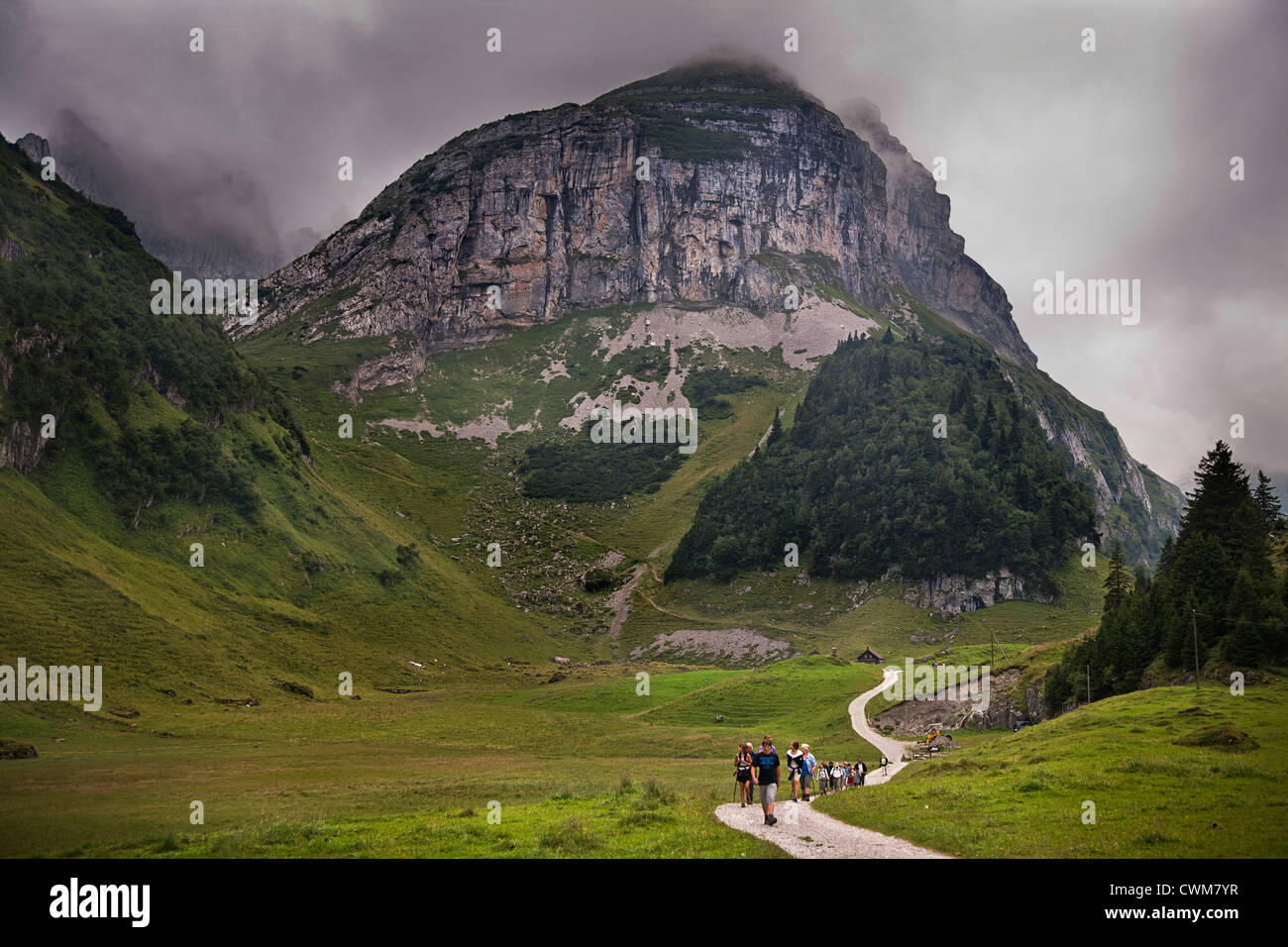 Europe. Switzerland. Alps. Engelberg. Tourist hikers in green valley. Low clouds over mountain. Stock Photo