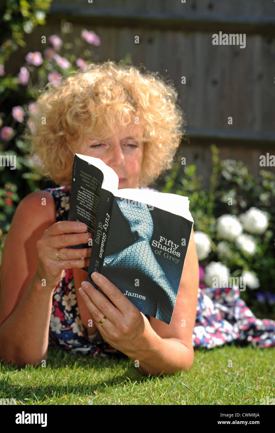 Mature woman in 50s reading sexy novel Fifty shades of Grey by E L James  while sitting in her garden UK Stock Photo - Alamy