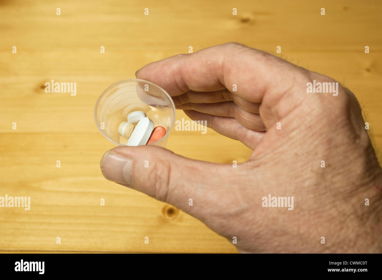 A man's hand holding a hospital medicines dispensing beaker containing ...