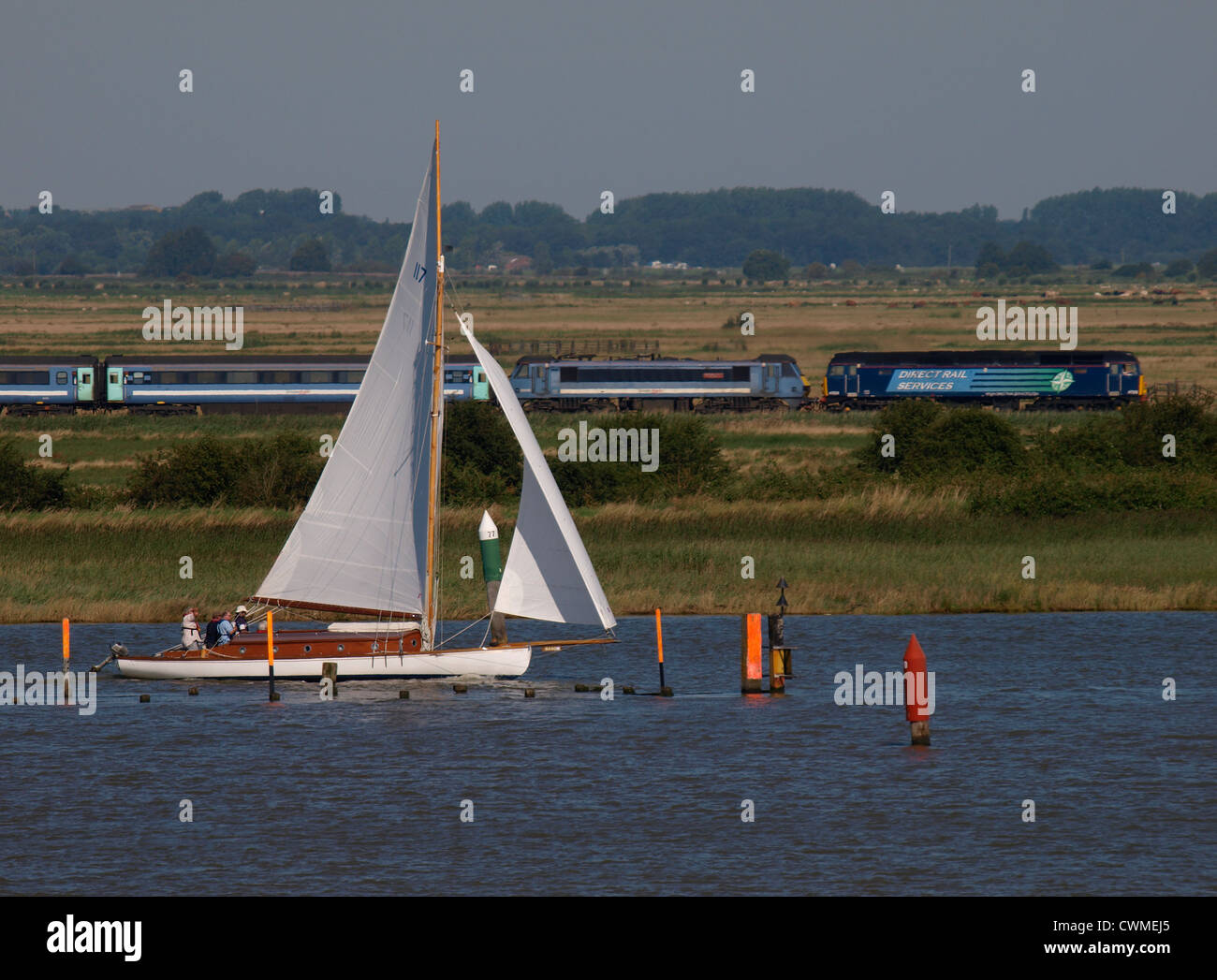 Yacht on the Norfolk Broads where the rivers Yare and Waveney meet, Direct rail services train in the background, UK Stock Photo