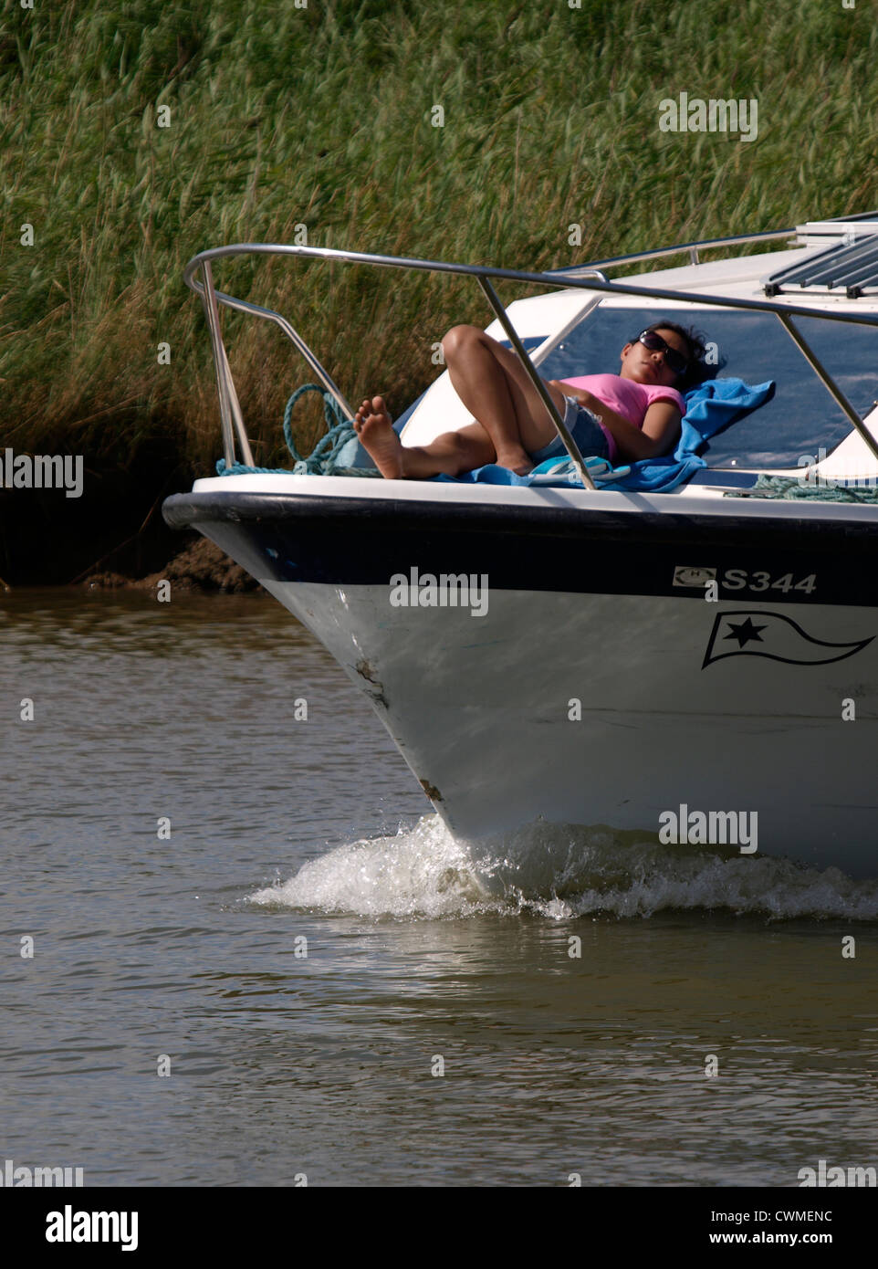 Child sunbathing on the front of a boat on the Norfolk Broads, UK Stock Photo