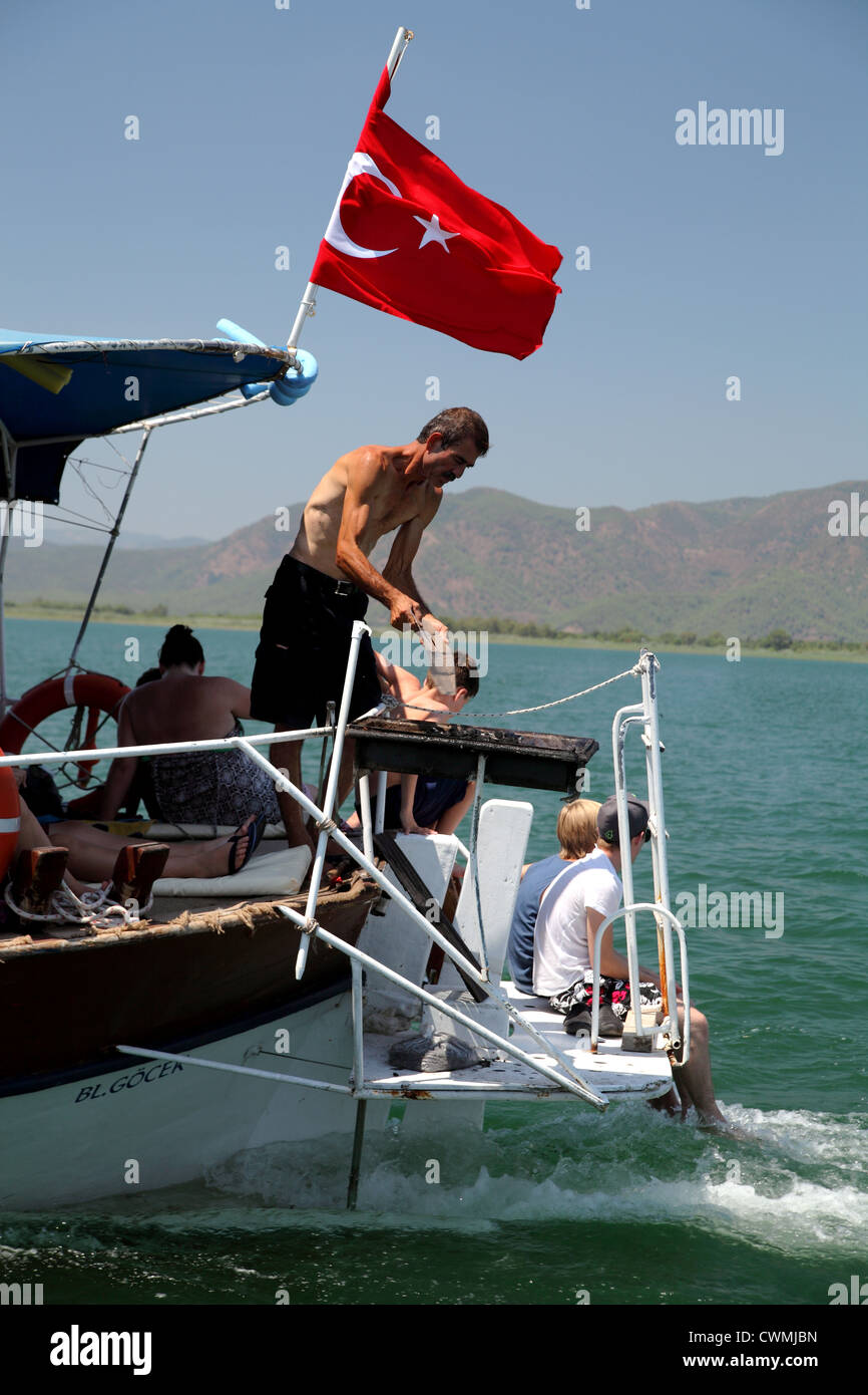 Turkish man preparing a barbecue situated at the stern of a tourist boat, near Dalyan Turkey; he is fanning coals with paper Stock Photo