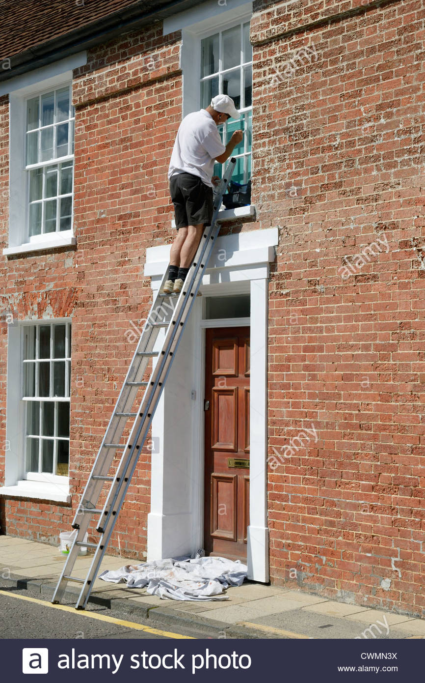 Workman up a ladder decorating sash window, West Street, Wimborne Stock