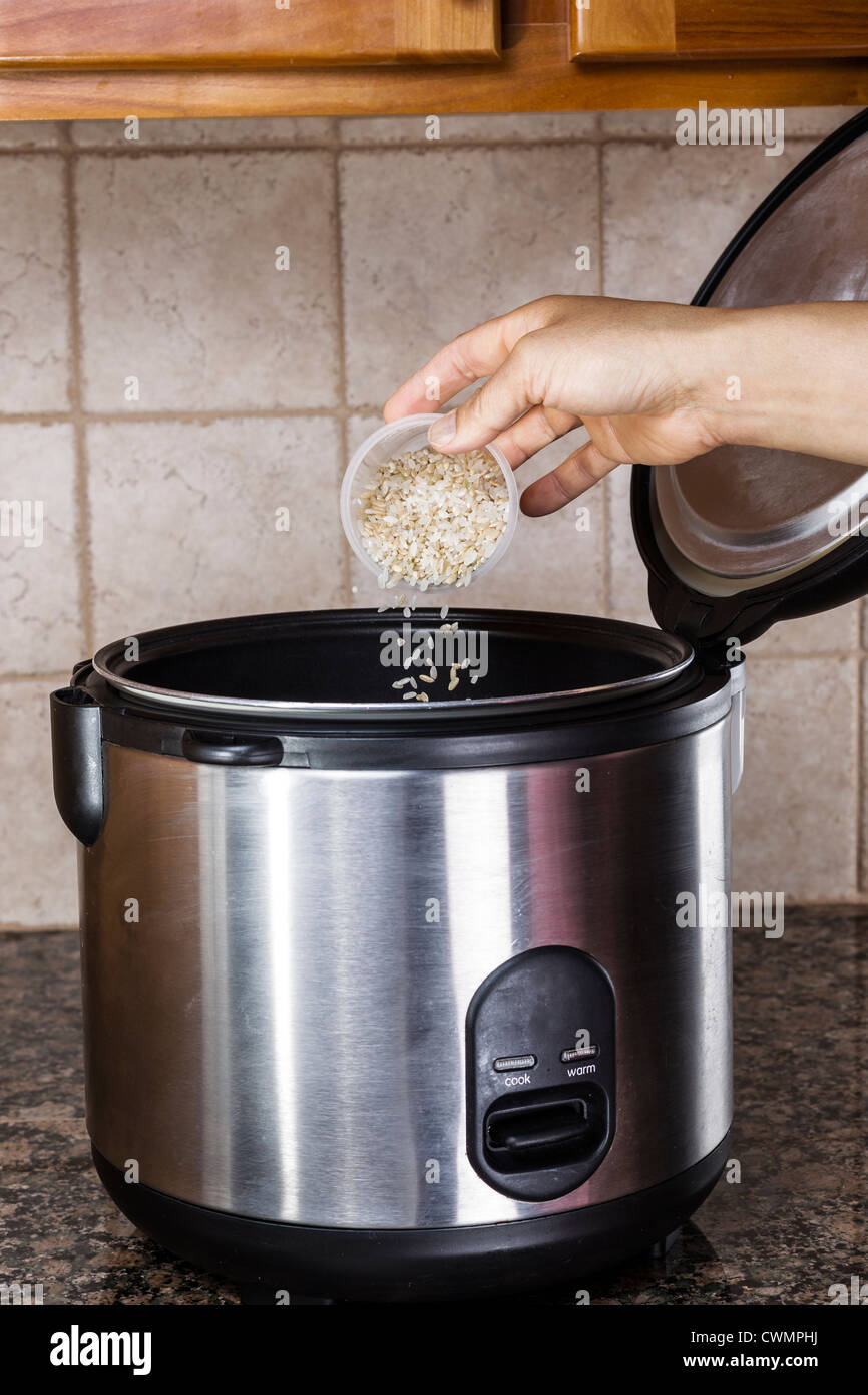 Hand pouring brown and white rice into rice cooker on stone counter top in kitchen Stock Photo