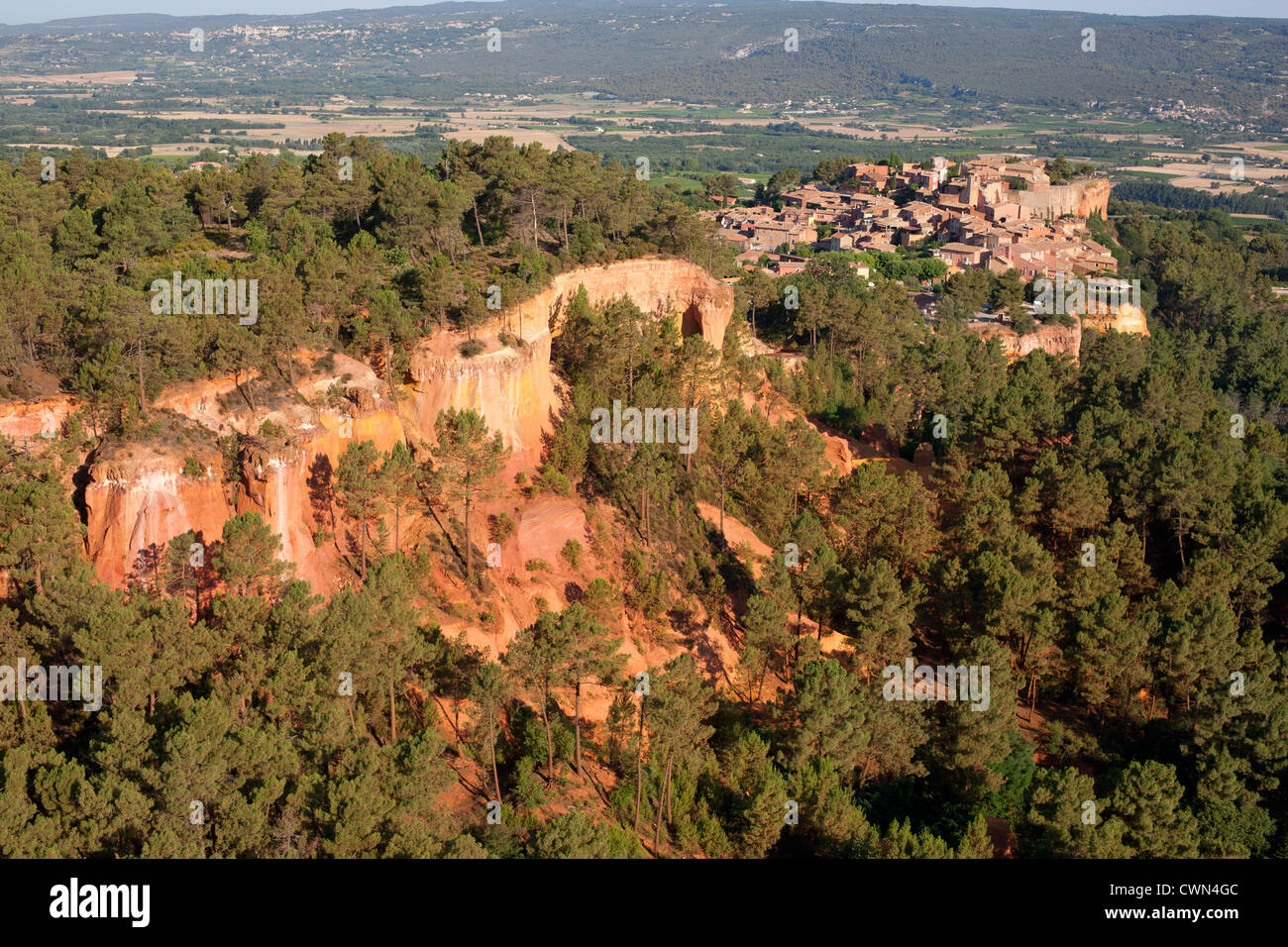 AERIAL VIEW. Medieval village perched on top of a red-ocher clay cliff. Roussillon, Vaucluse, Provence, France. Stock Photo