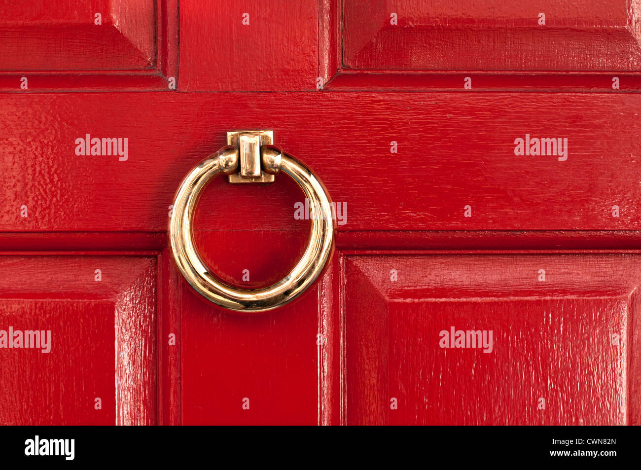 Shiny polished brass ring door knocker on red gloss painted door, London, England, UK Stock Photo
