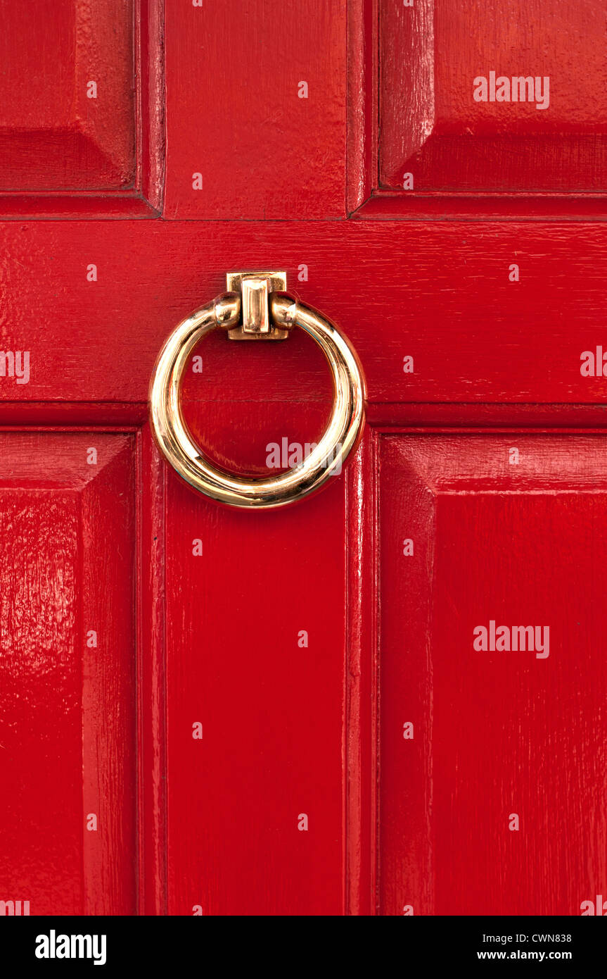 Shiny polished brass ring door knocker on red gloss painted door, London, England, UK Stock Photo