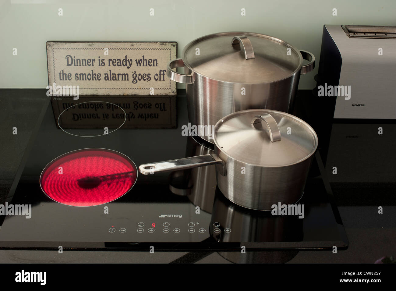 Stainless steel pans next to a burning ceramic cooking stove Stock