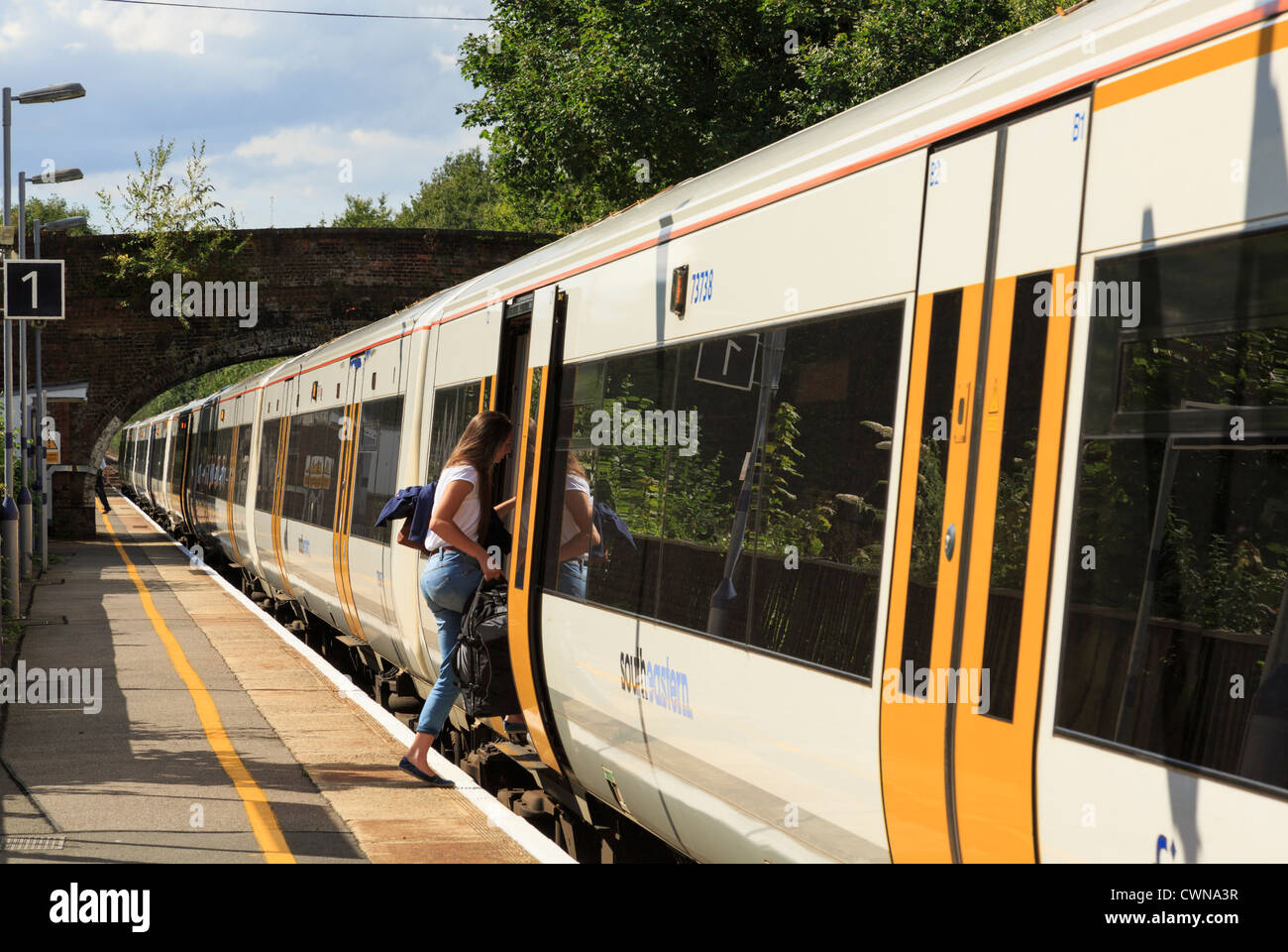 Female passenger boarding SouthEastern train commuting to London from platform in railway station at Pluckley Kent England UK Britain Stock Photo