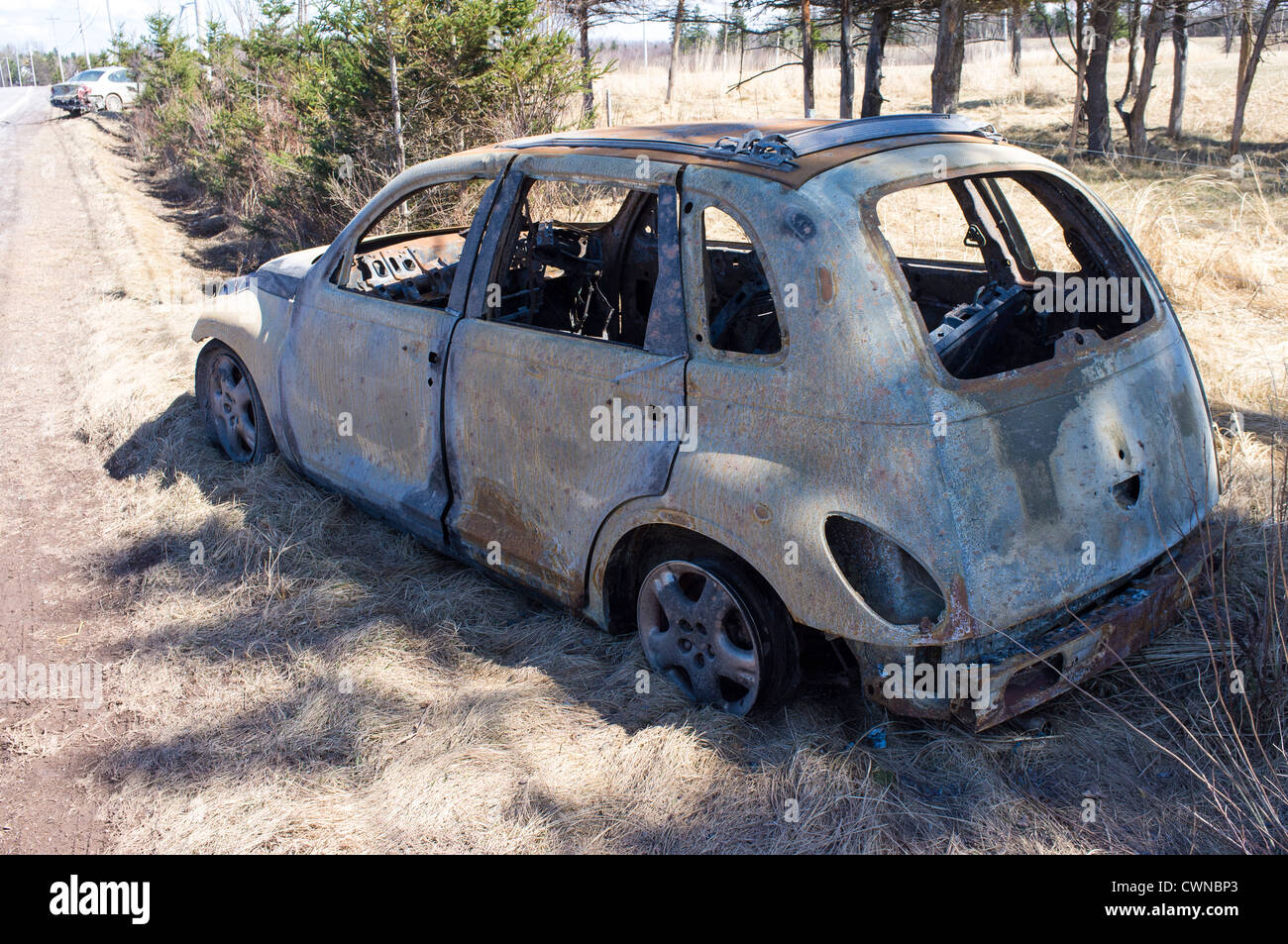 A burned out car sits on the side of a road after an accident. Stock Photo