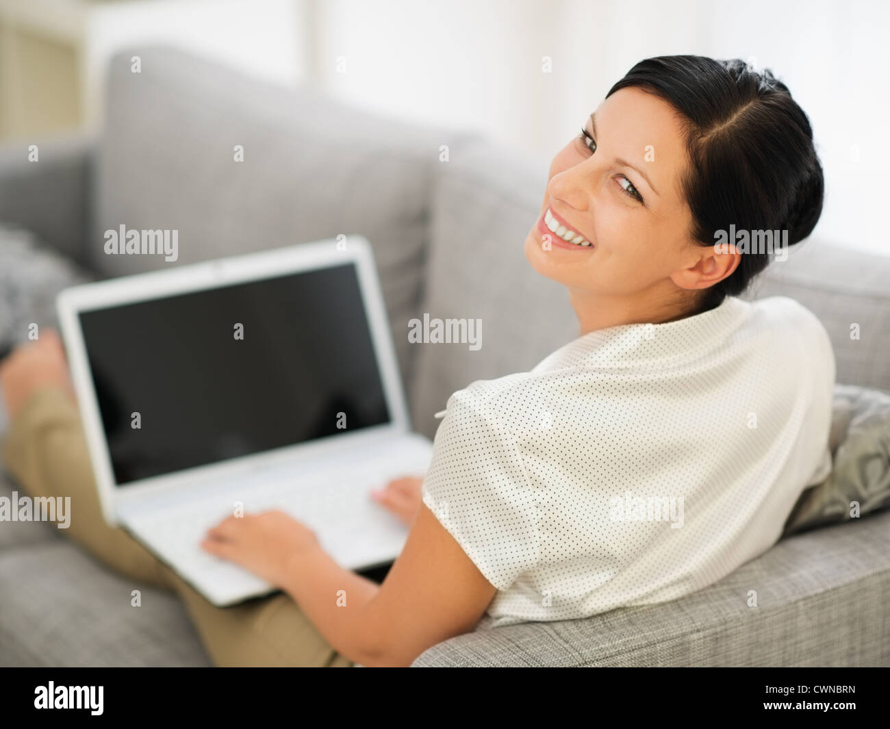 Smiling young woman laying on couch and working on laptop Stock Photo