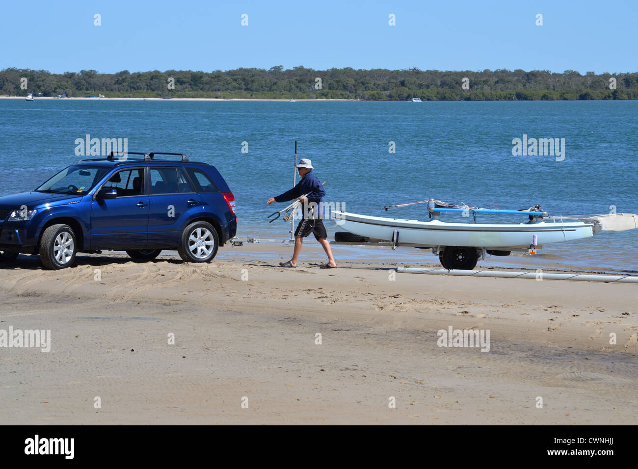 man with blue Suzuki Grand Vitara backs his sailboat into the water and unloads Stock Photo