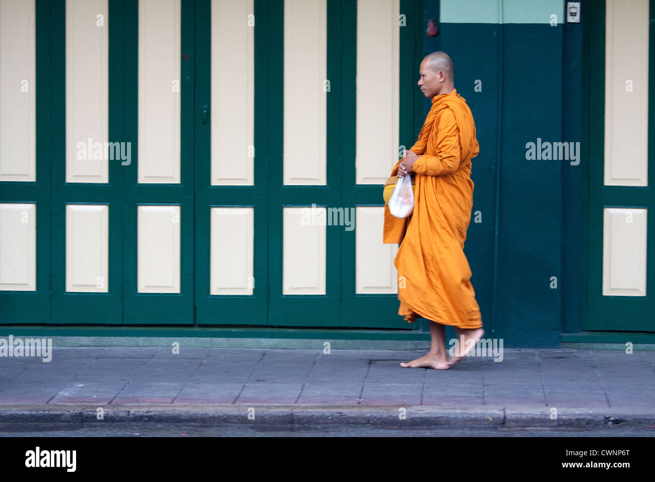 Thai Buddhist monk walking the streets of Bangkok in the early morning wearing traditional orange Buddhist robes and begging for alms. Stock Photo
