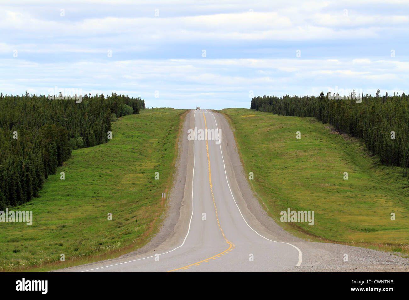 The Alaskan Highway as it goes through a Canadian forest with green grass and thick forestation. Stock Photo