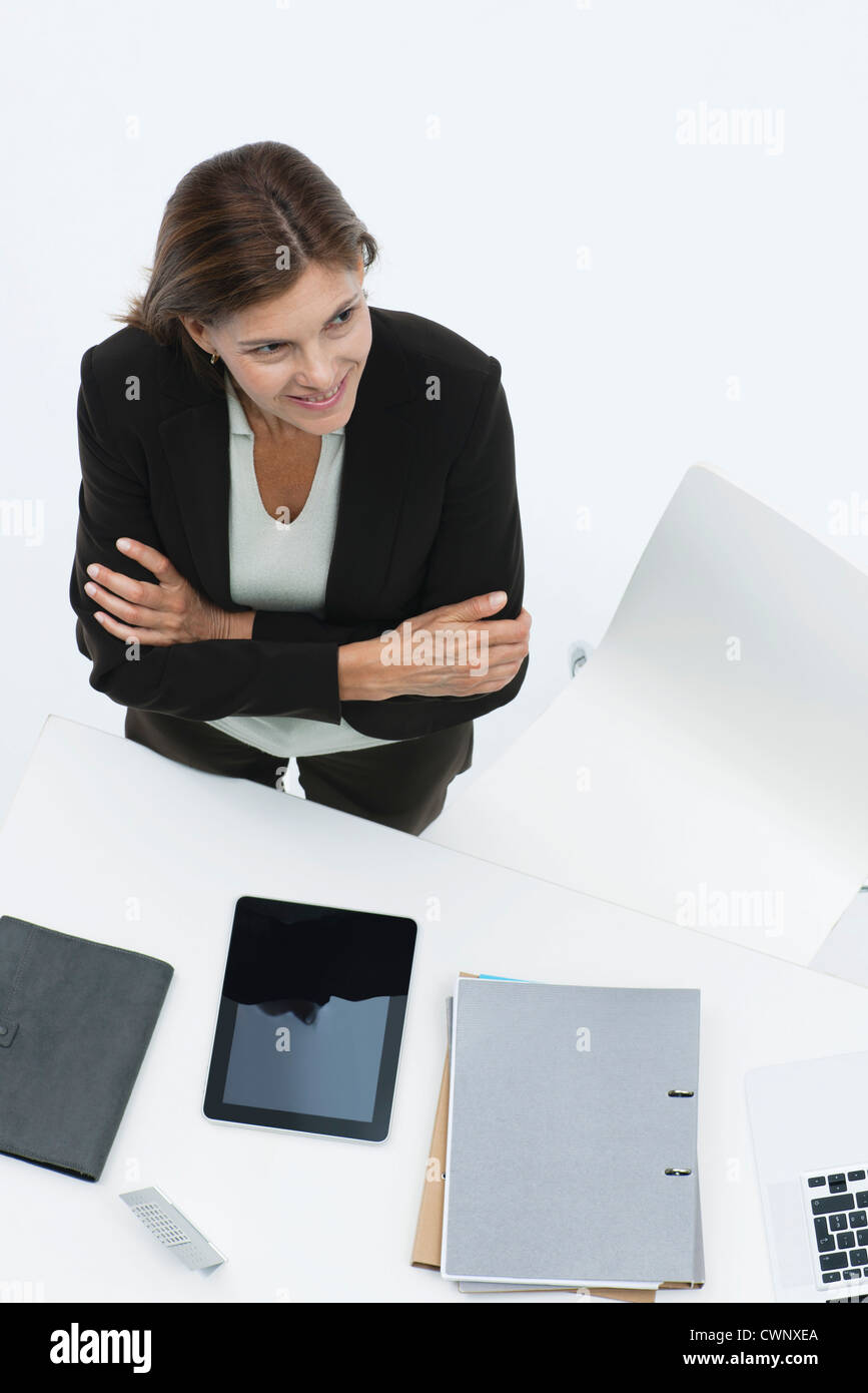 Businesswoman standing by desk with arms folding, high angle view Stock