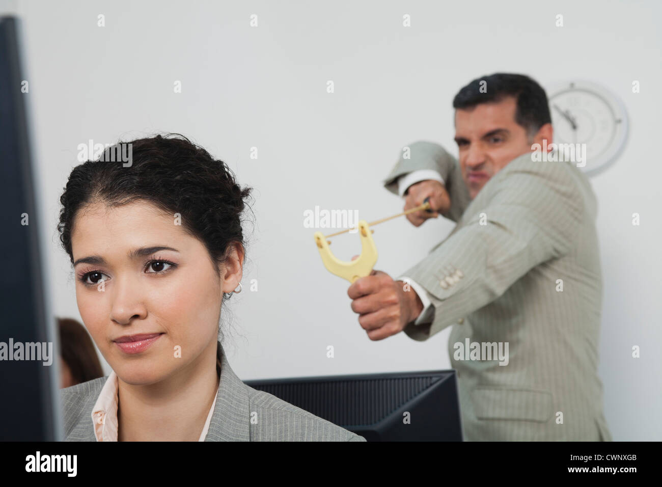 Businessman aiming slingshot at young female colleague Stock Photo Alamy