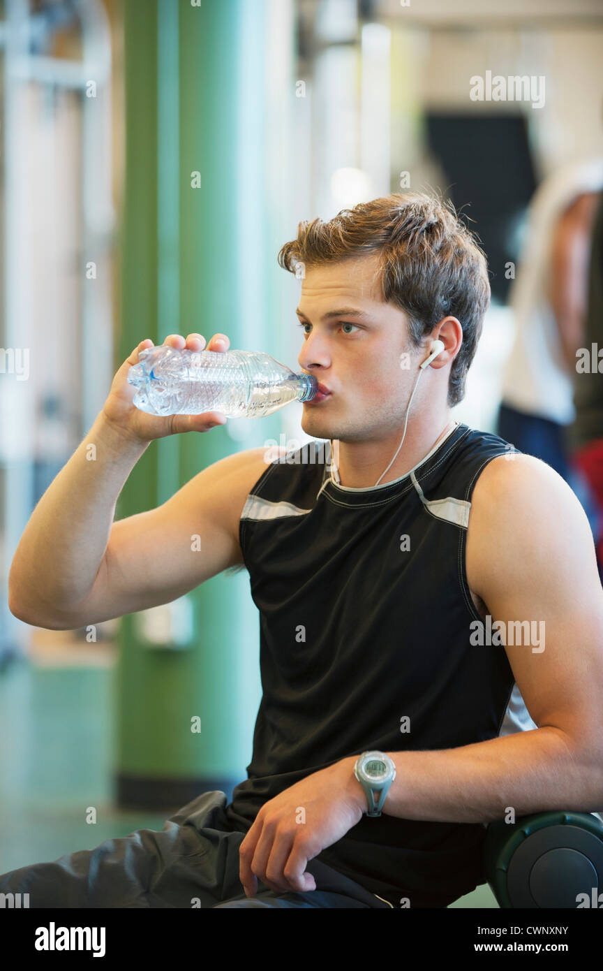 Young man drinking bottled water in gym room Stock Photo - Alamy