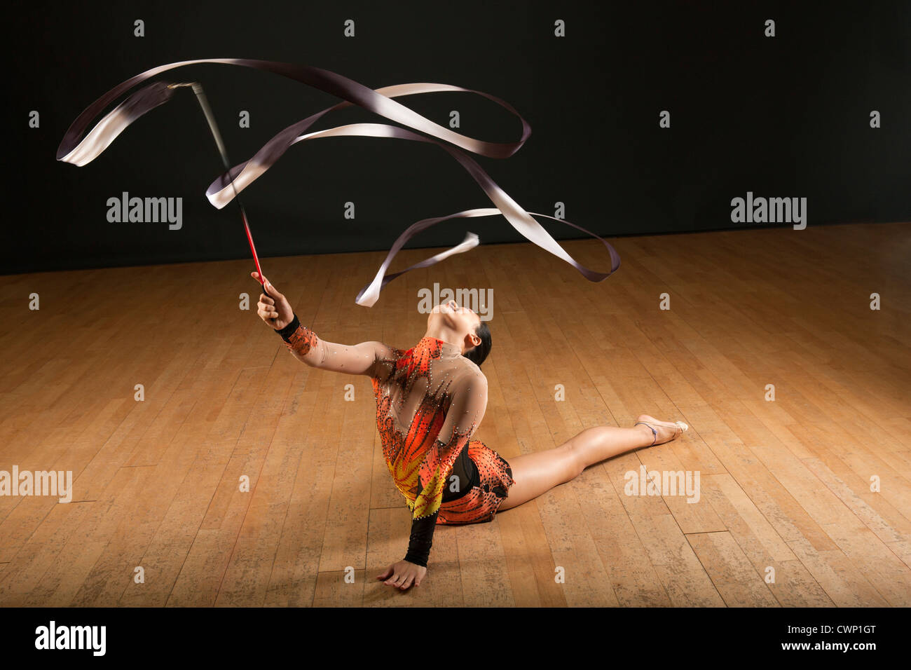 Gymnast bending backwards on floor, twirling ribbon Stock Photo