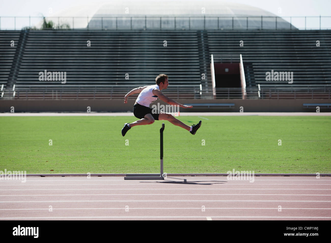 Male athlete clearing hurdle, side view Stock Photo