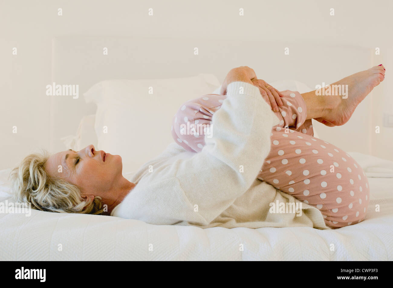 Mature woman lying on bed in fetal position Stock Photo