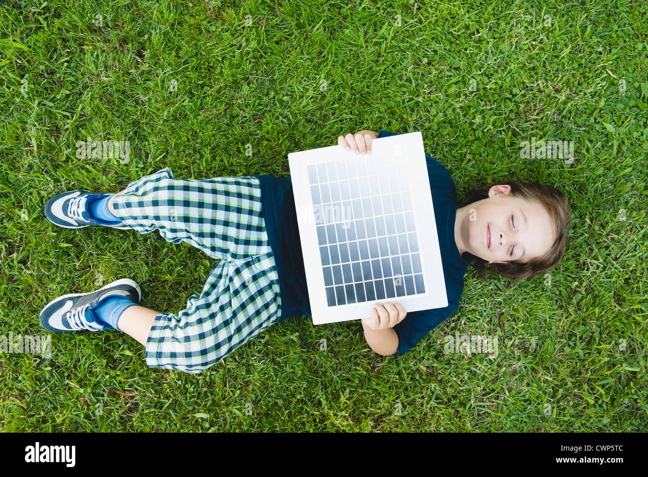 Boy lying on grass holding solar panel Stock Photo