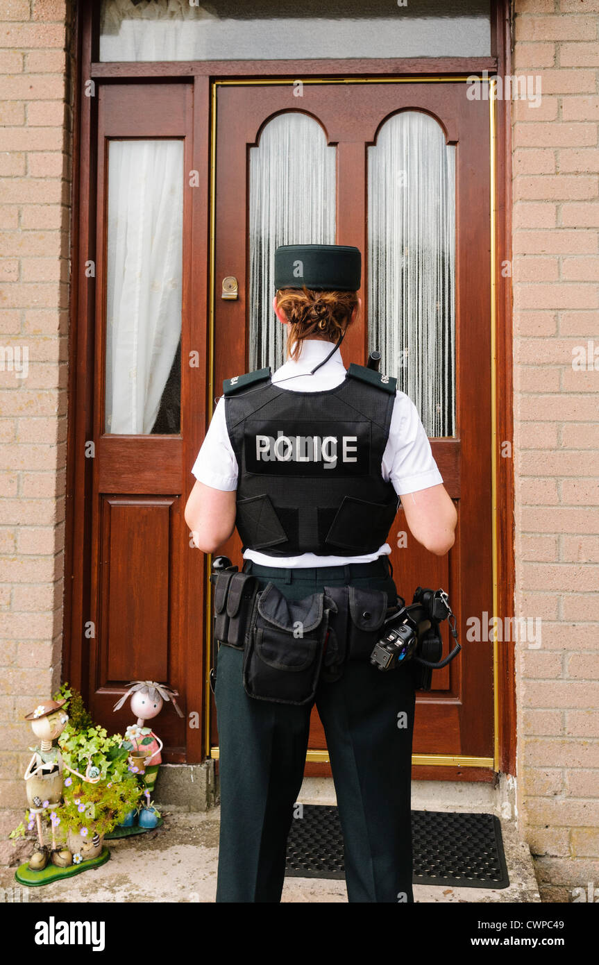 Police woman waits at the front door of a house Stock Photo