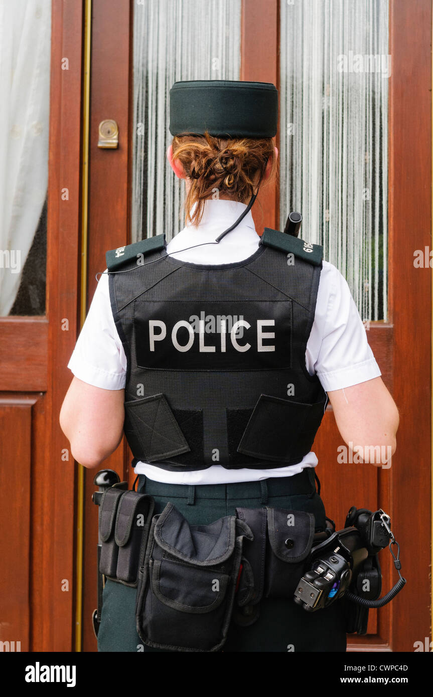 Police woman waits at the front door of a house Stock Photo