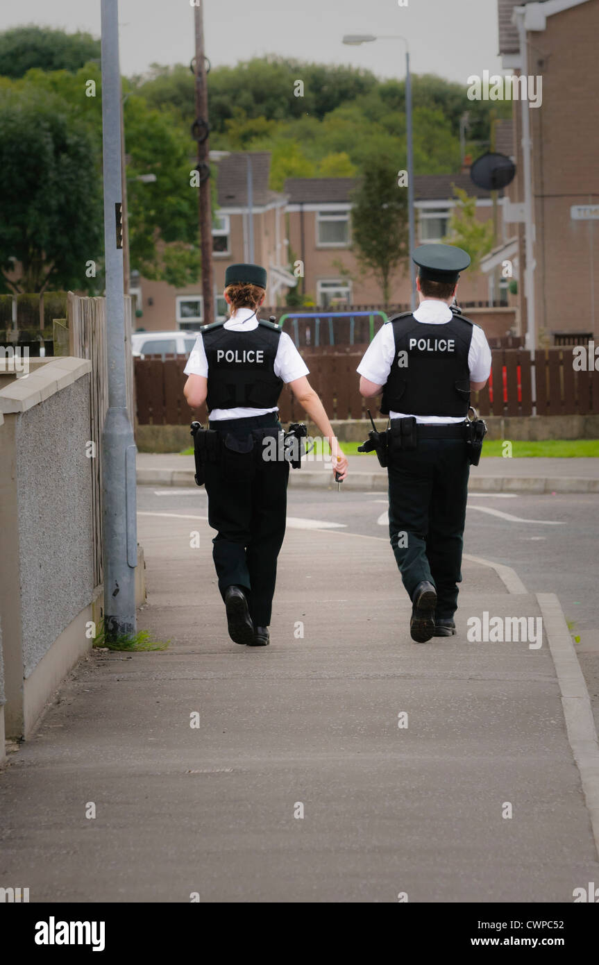 Female and male police officers walking along the footpath of a street in a residential area (vignetted) Stock Photo