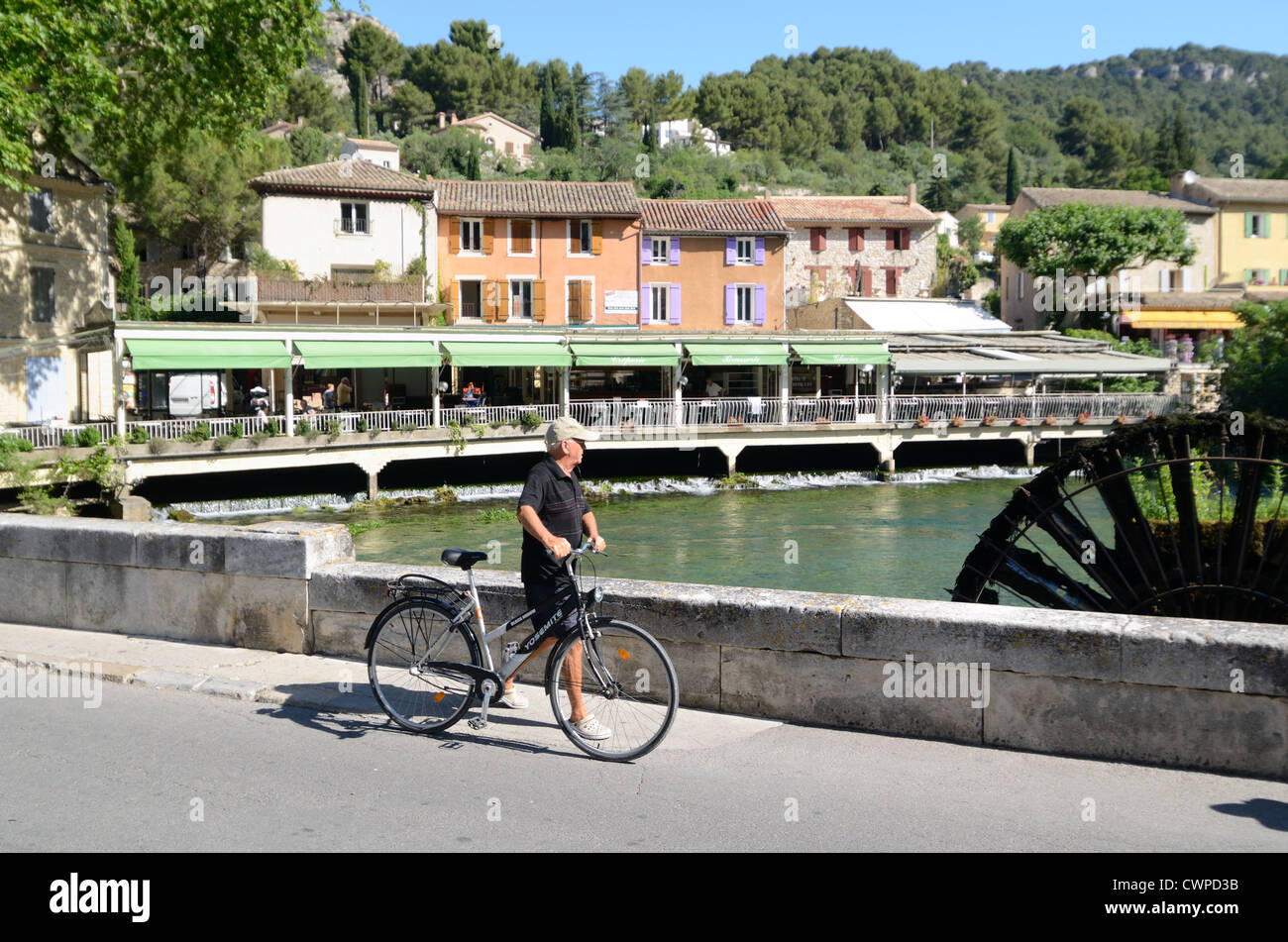 Cyclist Walks Past Riverfront Restaurants & over Bridge over River Sorgue at Fontaine-de-Vaucluse Vaucluse Provence France Stock Photo