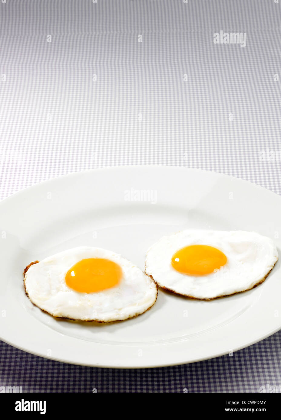 Two fried eggs with yellow yokes on white plate with gingham tablecloth Stock Photo