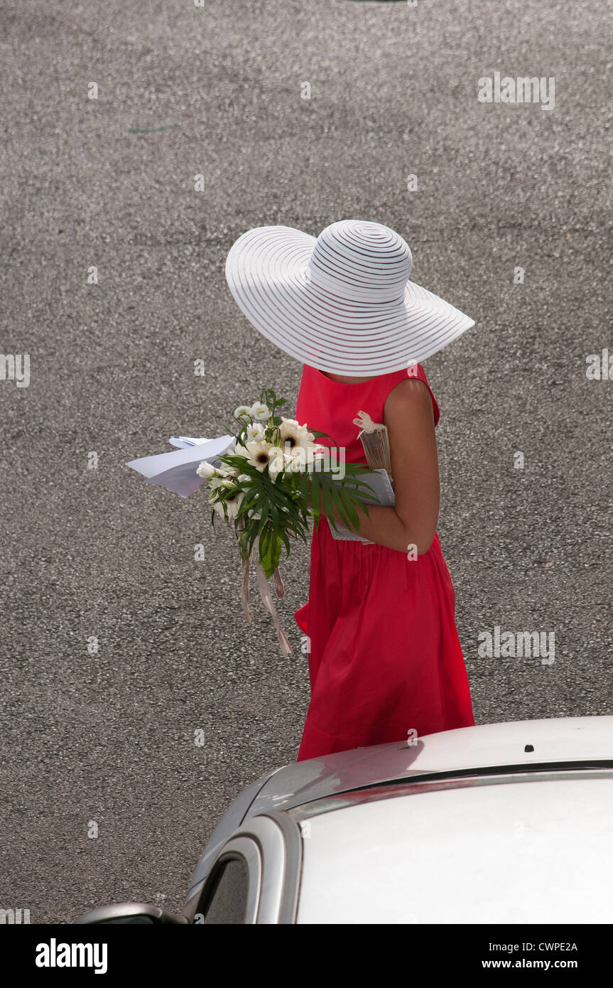 Wedding guest wearing a white hat and carrying a bouquet of flowers Stock Photo