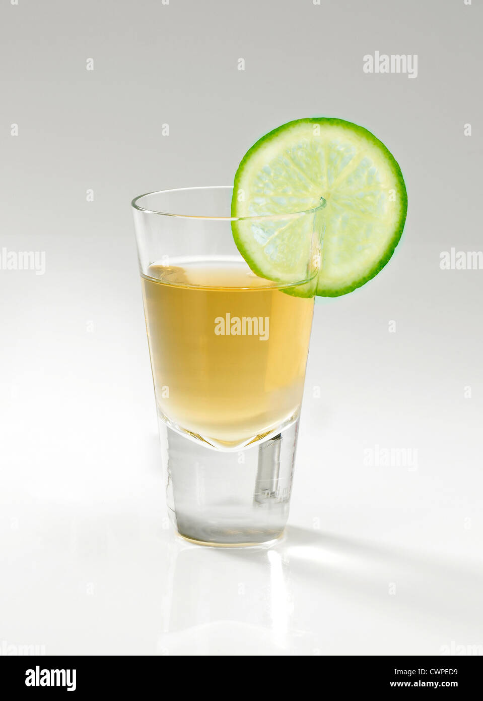 A shot glass of Tequila and a slice of Lime on a graduated grey background Stock Photo