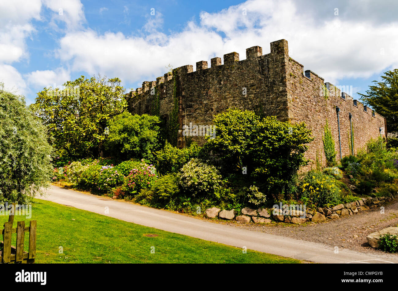 Trees and shrubs form an attractive border around tall crenelated stone walls enclosing the restaurant at Muncaster Castle Stock Photo