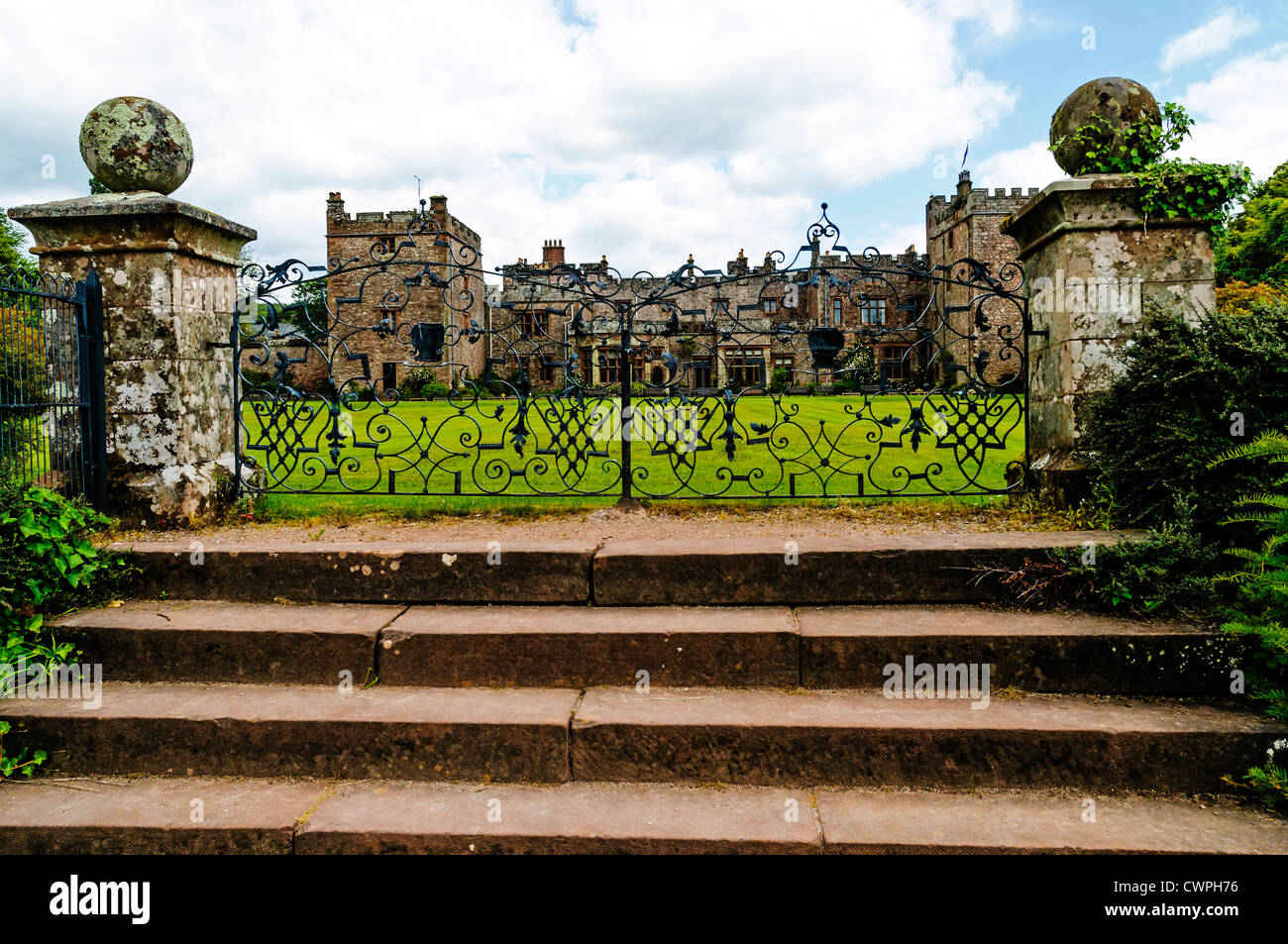 The lawn and facade of Muncaster Castle with two crenelated square towers seen through the patterns of the wrought iron gates Stock Photo