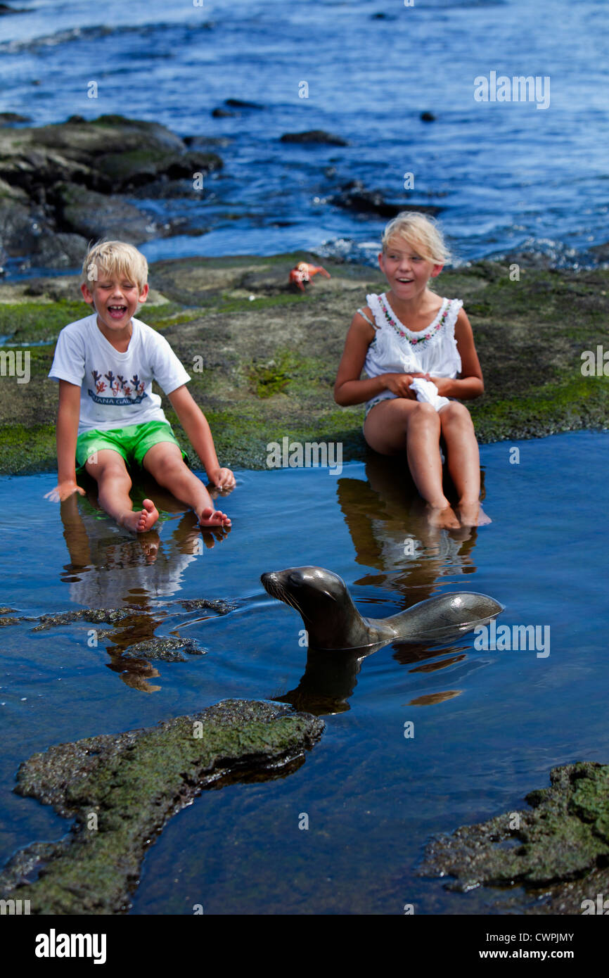 Young sea lion playing with children, Puerto Egas, James Island, the Galapagos, Ecuador Stock Photo