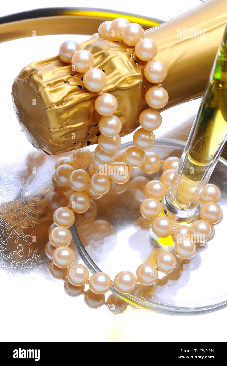 Closeup of a glass of champagne with a bottle on its side and a string of pearls draped over the neck of the bottle. Stock Photo