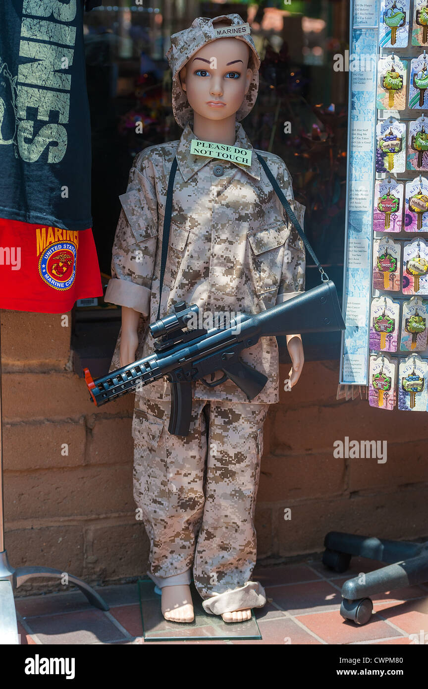 A display of a child life size doll, dressed in camouflage uniform and toy machine gun at the entrance to a souvenir shop in San Stock Photo